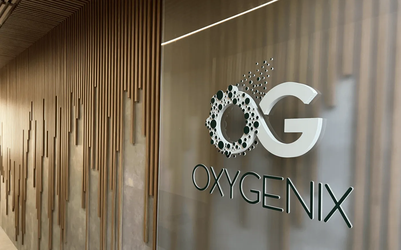 Recepção da Oxygenix — logo 3D sobre vidro fosco e painel de madeira ripada
